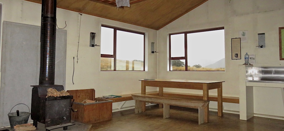 There's an indoor table and a view out to the setting sun. | Sylvester Hut, Kahurangi National Park