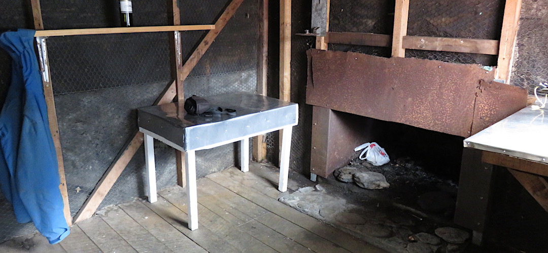 The open fireplace, and bench. | Cedar Flats Historic Hut, Toaroha River, West Coast