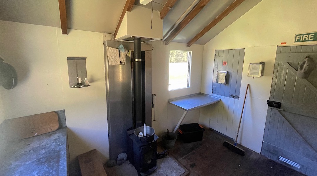 Two benches and a small woodburner.  |  Lees Creek Hut, Lees River, Marlborough